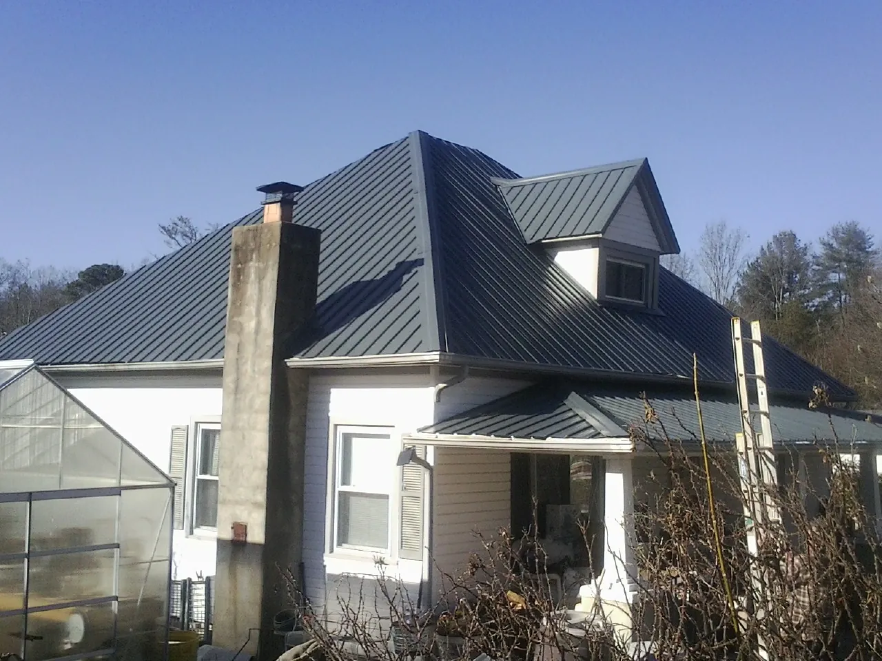 Dark blue standing seam metal roof on a white farmhouse with dormer — Slate & Tile Roof Repair by Roofing Brothers in Newkirk