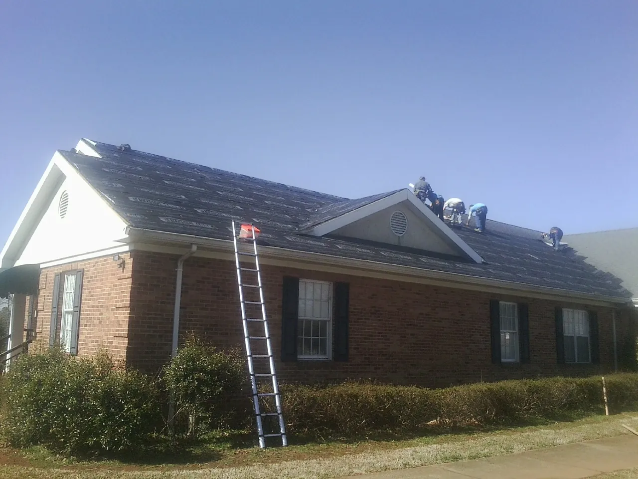 Crew tearing shingles off a brick ranch roof with a ladder set — Metal Roof Repair work by our crew in Newkirk