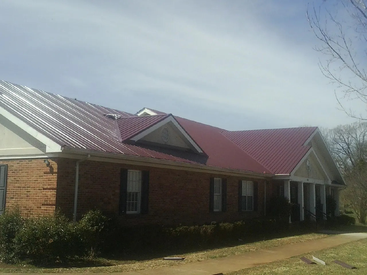 Red metal roof with gabled entries on a long brick building, from a Hail Damage Roof Repair job in Newkirk