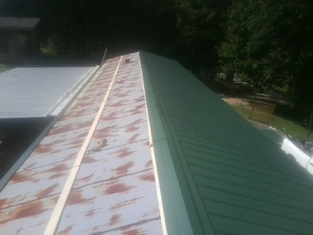 Old rusted panels beside newly installed green metal roofing — Wind Damage Roof Repair by Roofing Brothers in Newkirk
