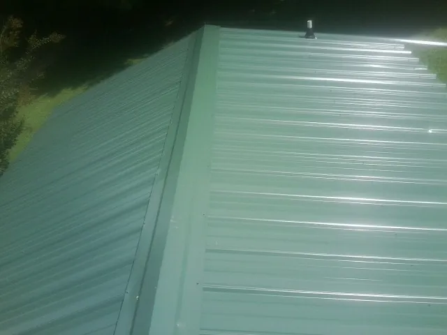 New green metal panels meeting at the ridge of a roof — Flat Roof Repair work by our crew in Newkirk