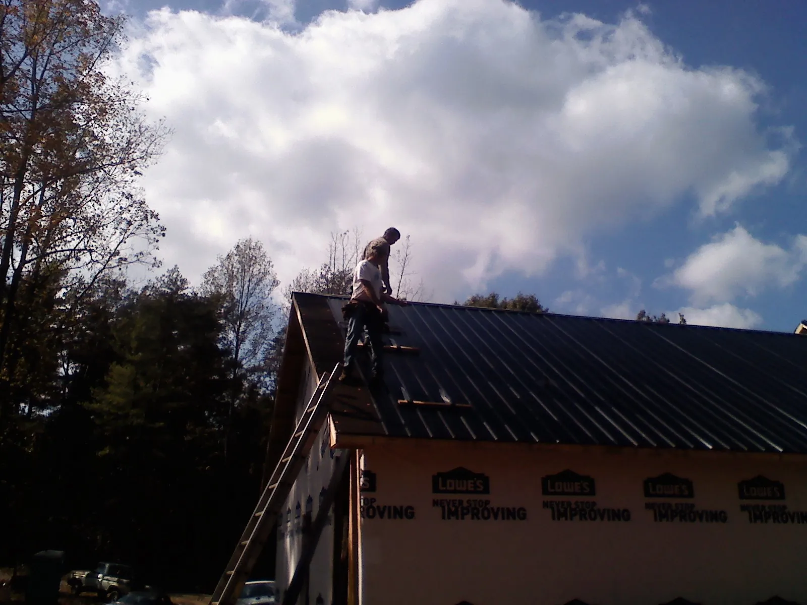 Roofer fastening dark metal panels high against a cloudy sky, from a Roof Inspection job in Newkirk