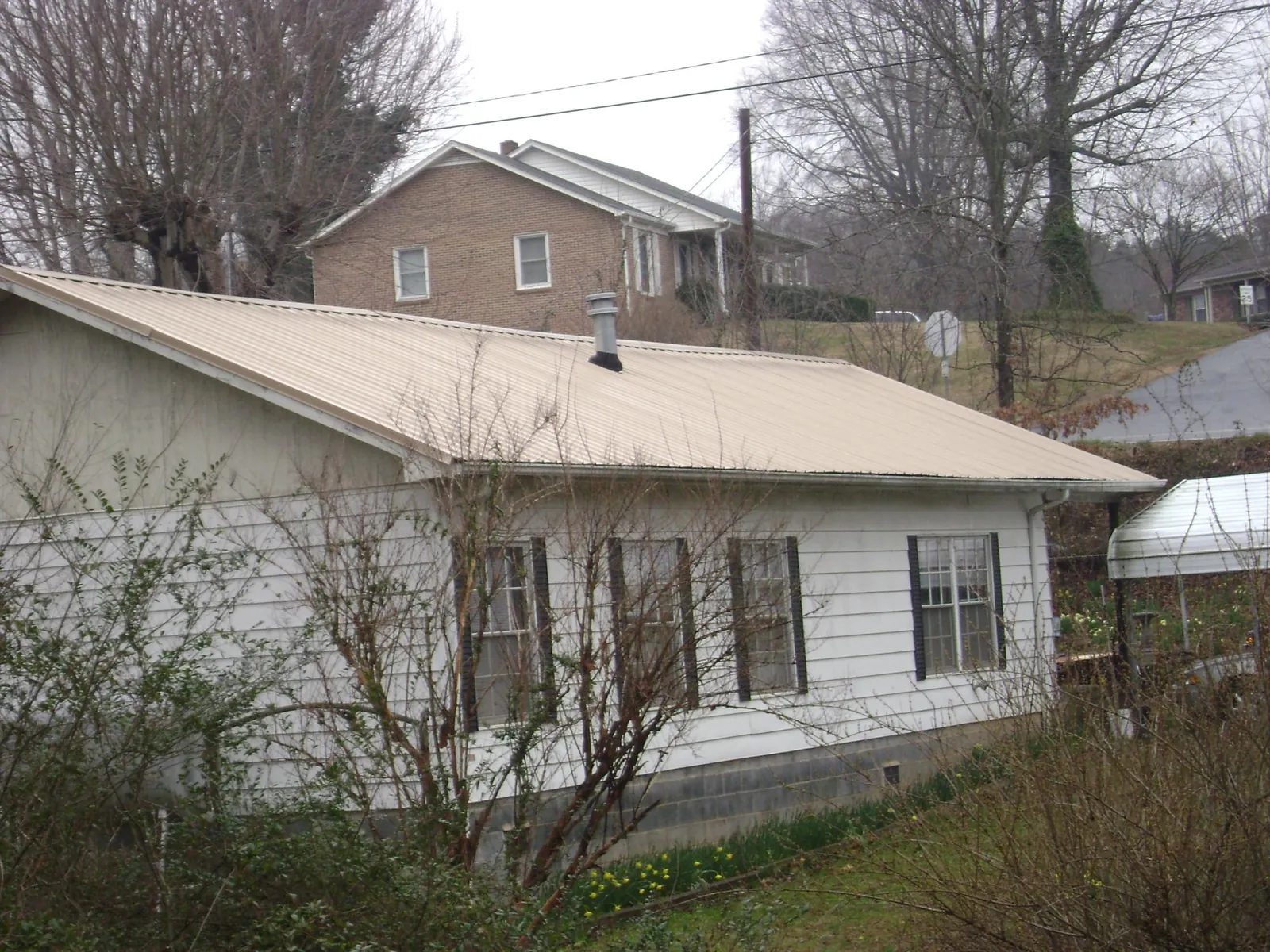 Tan metal roof on a white sided house set into a hillside — Commercial Roofing by Roofing Brothers in Newkirk