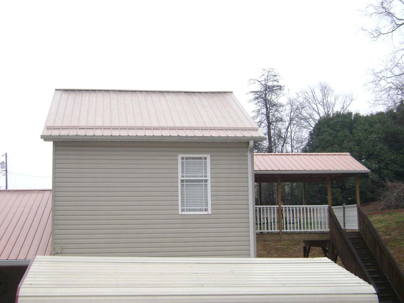 Tan metal roofs on a two story addition and attached porch, from a Roof Replacement job in Newkirk